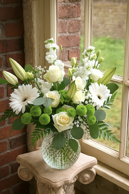Sympathy flowers in white and green tones for delivery in Maple Ridge. Garden-style bouquet with roses, lisianthus, lilies and chrysanthemums in a clear glass vase.